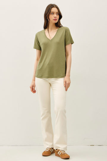 woman wearing a green short sleeve v-neck t-shirt and white flared jeans with brown sneakers