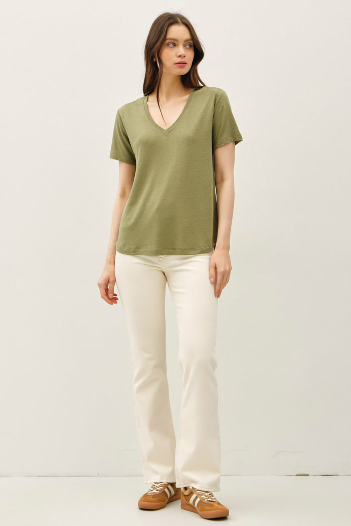 woman wearing a green short sleeve v-neck t-shirt and white flared jeans with brown sneakers