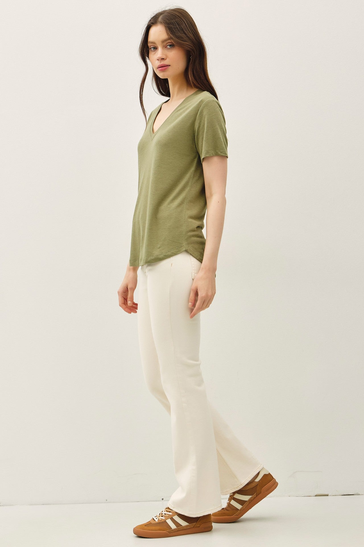 woman wearing an olive green v-neck t-shirt and white flared pants, styled with brown sneakers