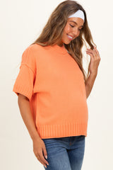 woman wearing a bright orange short sleeve maternity sweater with a relaxed fit and a visible baby bump
