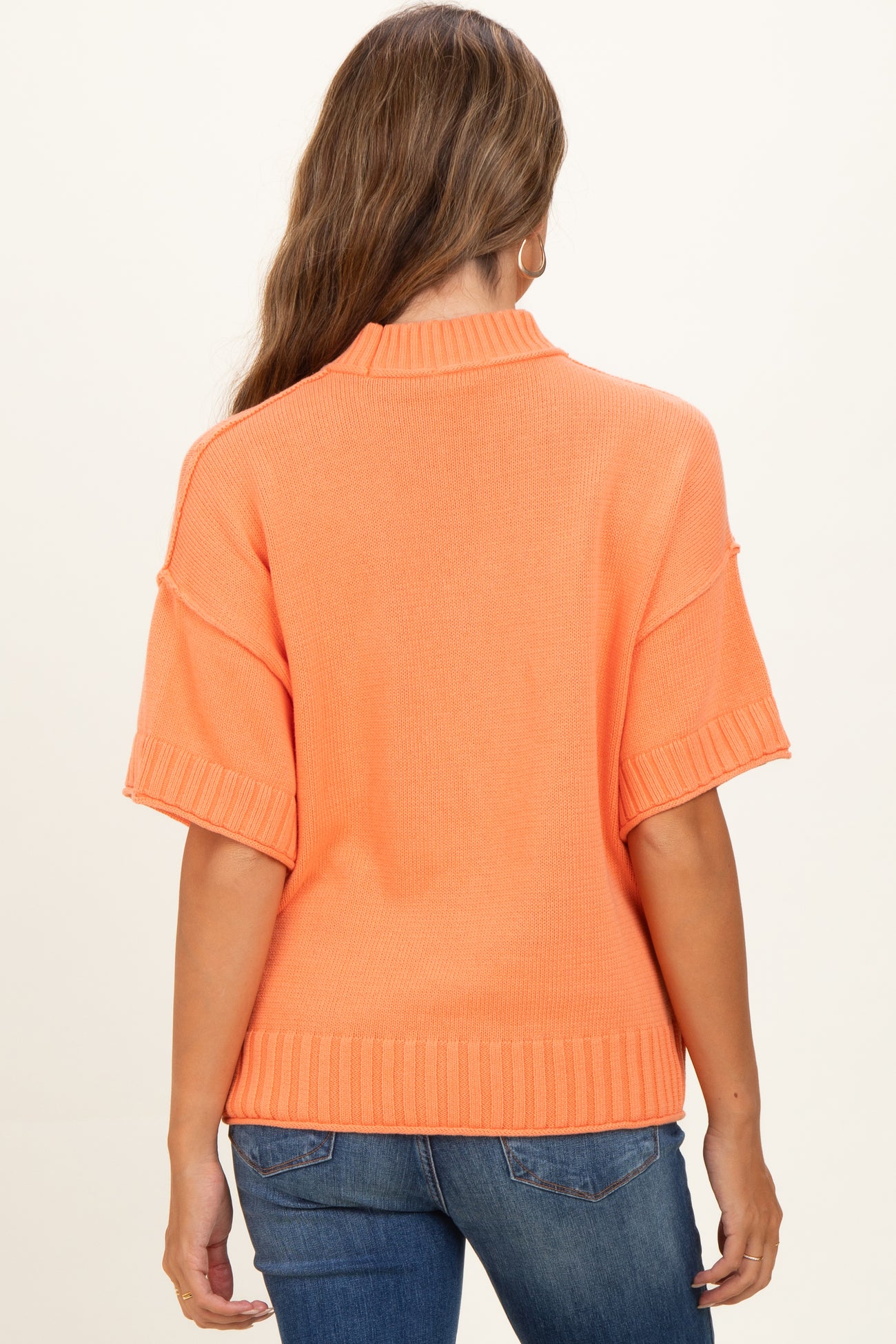 woman wearing an orange short sleeve knit maternity sweater with a relaxed fit and ribbed details