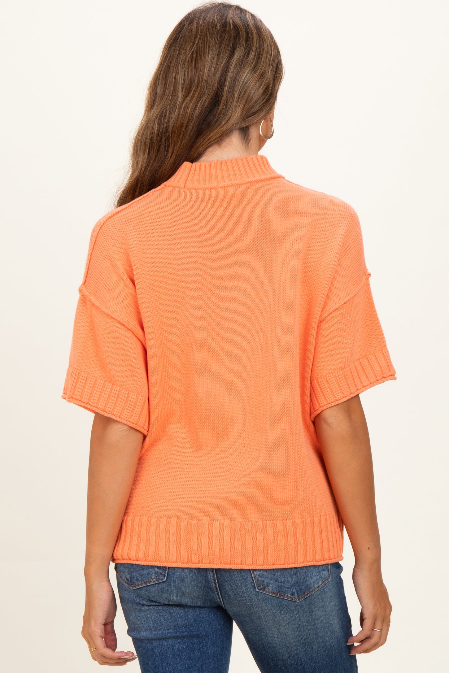 woman wearing an orange short sleeve knit maternity sweater with a relaxed fit and ribbed details
