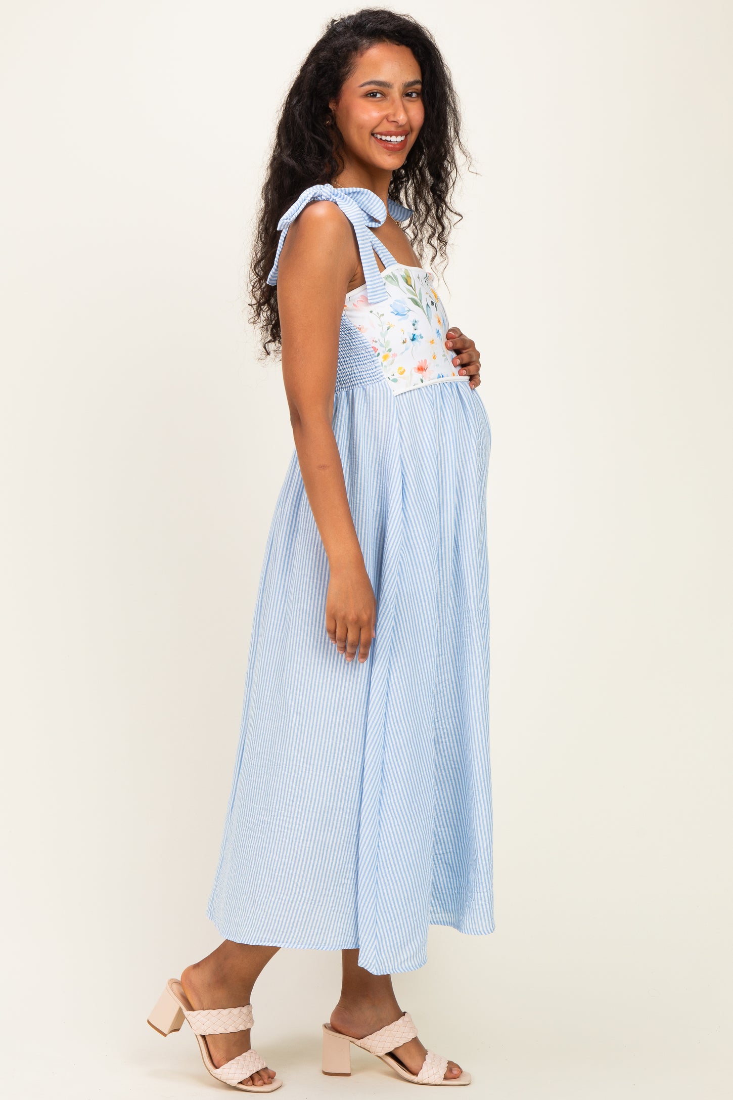 woman wearing a blue and white striped maternity dress with floral detailing and straps, showing her baby bump