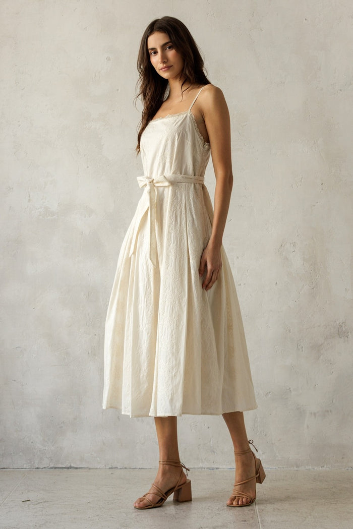 woman wearing an off-white sleeveless midi dress with a belted waist and full skirt, styled with tan block-heel sandals