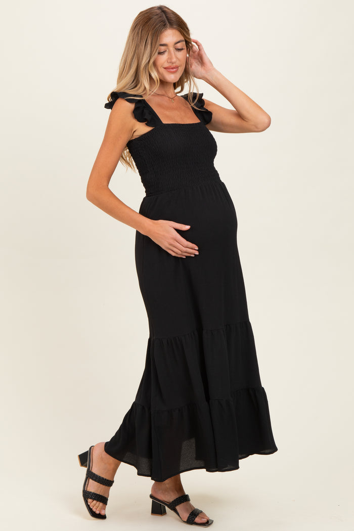 woman wearing a black maternity maxi dress with ruffled straps and a fitted bodice, showing her baby bump