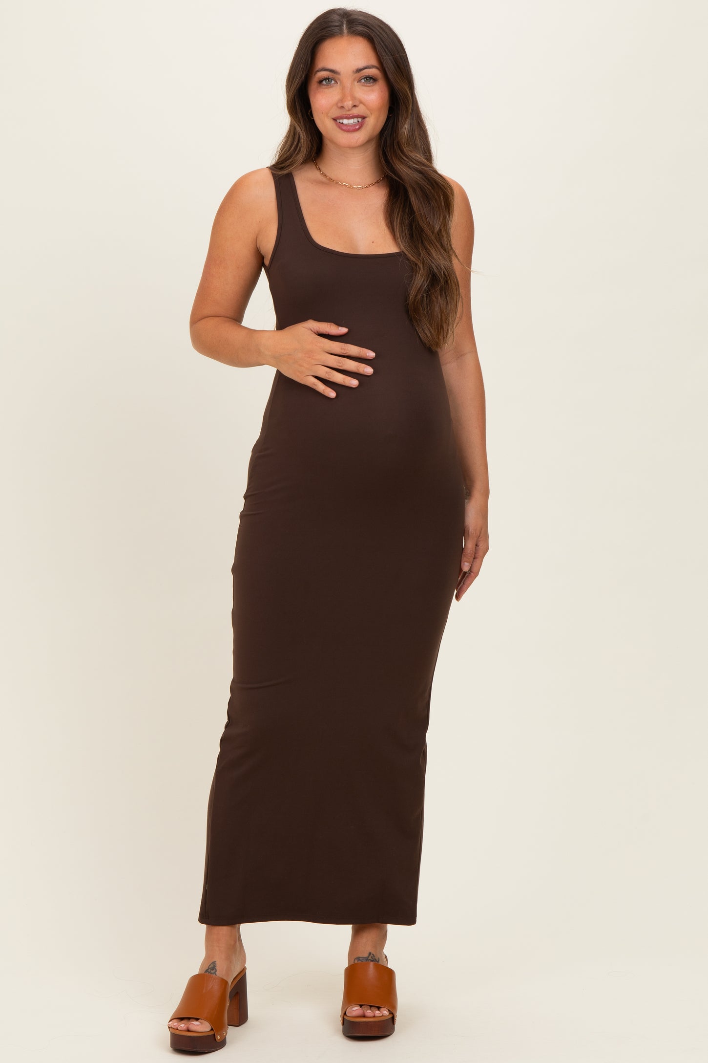 woman wearing a brown sleeveless maxi maternity dress and holding her baby bump