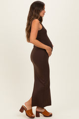 woman wearing a brown sleeveless maternity dress and gently holding her baby bump, standing sideways