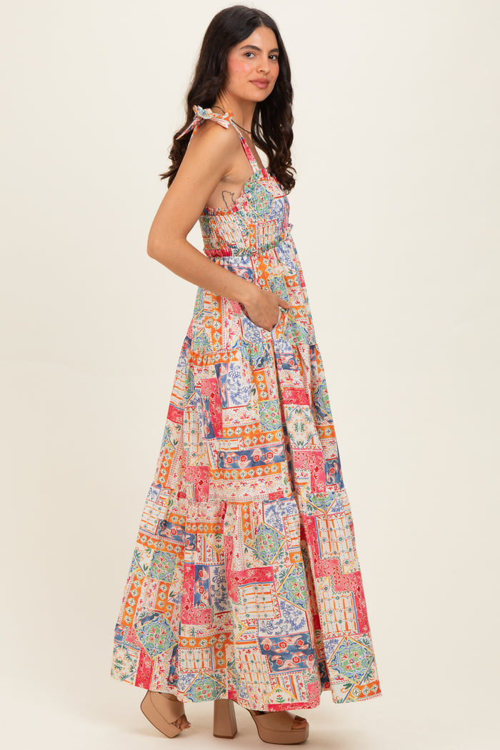 woman wearing a colorful patterned maxi dress with smocked bodice and pockets, standing in a side profile