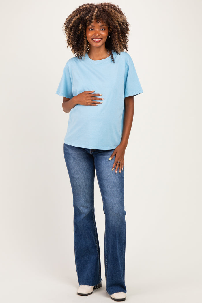woman wearing a light blue maternity t-shirt and blue flared jeans, gently holding her baby bump