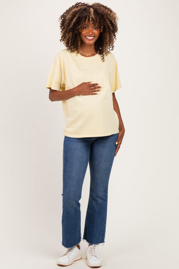 woman wearing a yellow short sleeve maternity top and blue jeans, holding her baby bump