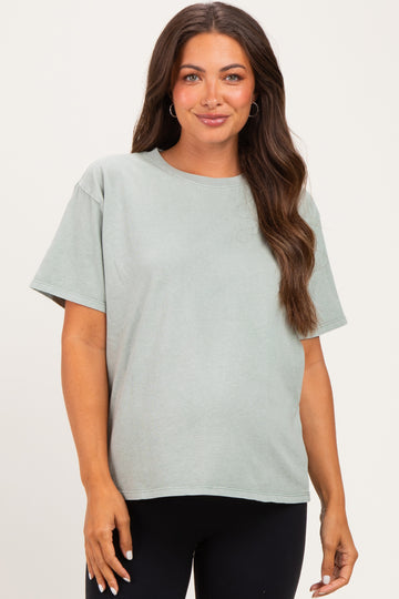 woman wearing a light green short sleeve maternity top with a relaxed fit, standing and smiling