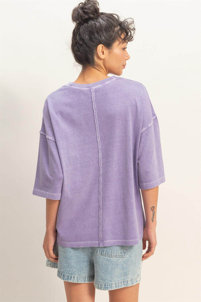 woman wearing a loose-fitting lavender purple oversized t-shirt and denim shorts, viewed from the back