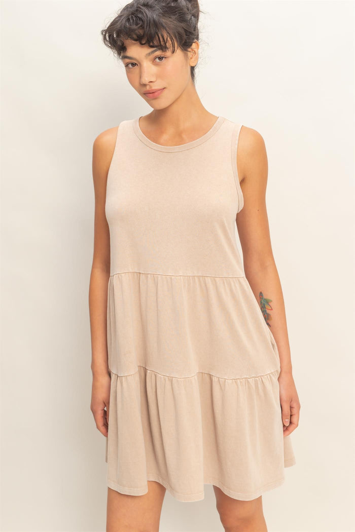 woman wearing a sleeveless beige tiered dress with a loose fit and round neckline