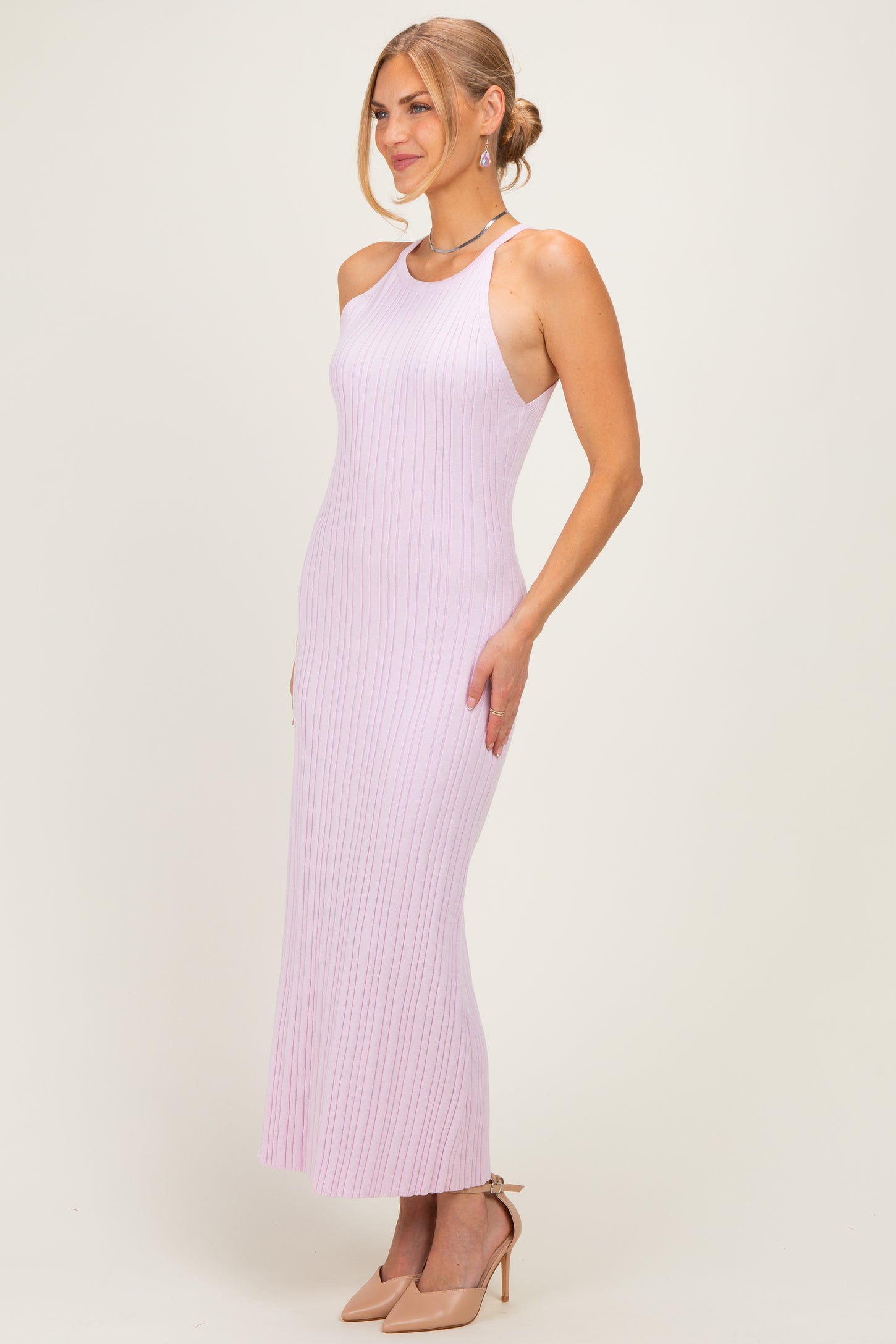 woman wearing a light pink ribbed maxi dress with a halter neckline and side slit, styled with nude heels