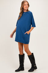woman wearing a blue oversized maternity dress with pockets and walking confidently, showcasing her baby bump
