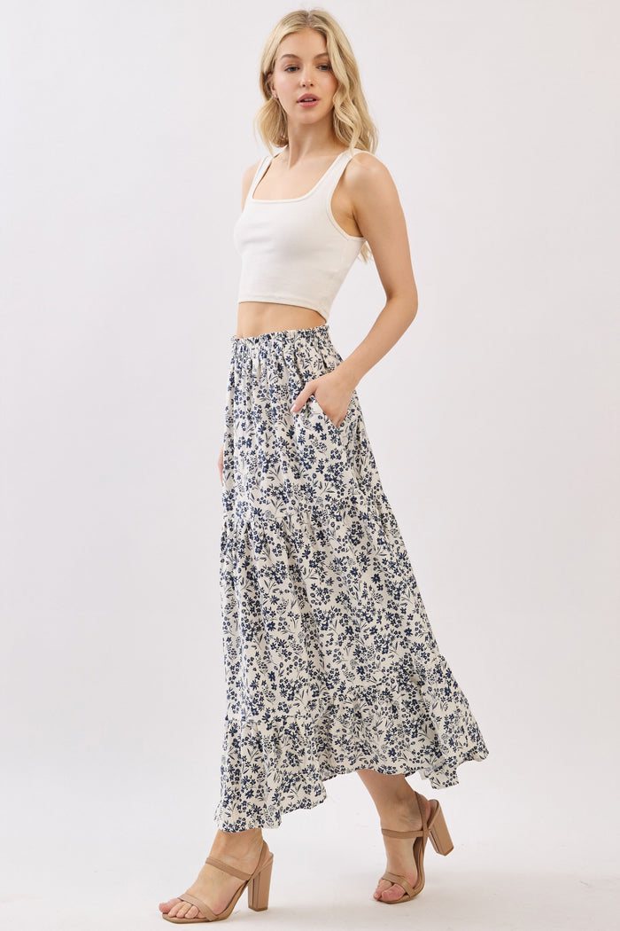 woman wearing a white crop top and a floral maxi skirt with pockets, standing on a light background