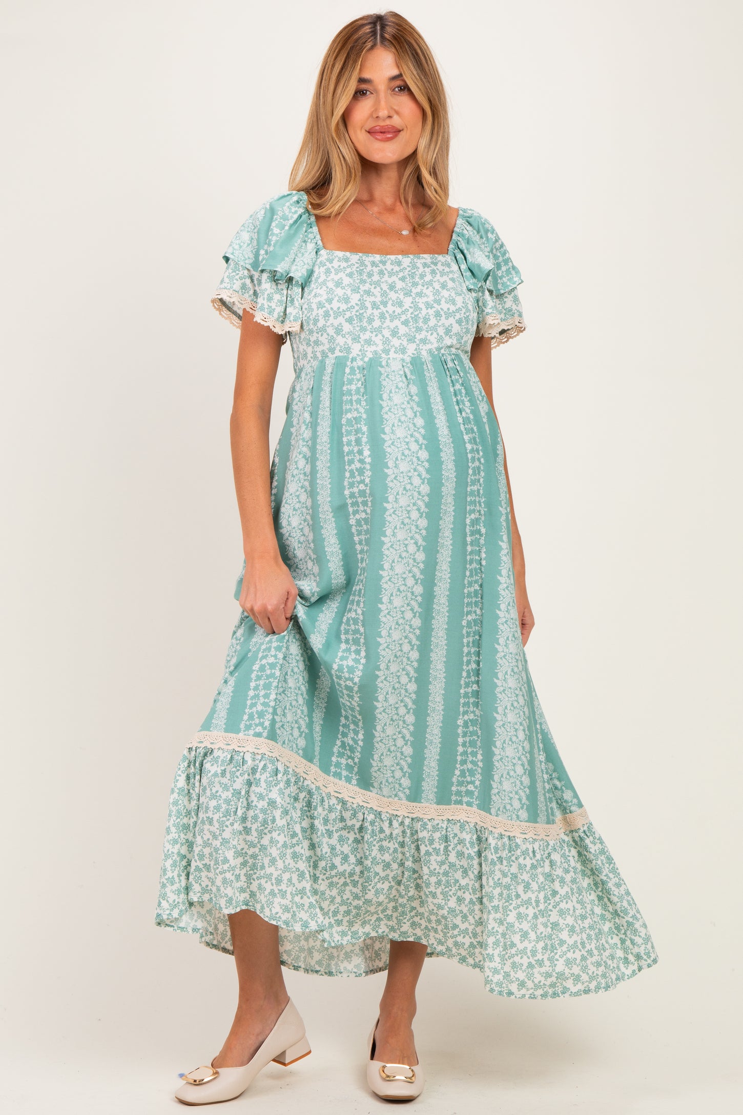 woman wearing a teal floral print maternity dress with short ruffled sleeves and a tiered hem, showing her baby bump