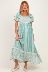 woman wearing a teal floral print maternity dress with short ruffled sleeves and a tiered hem, showing her baby bump