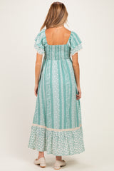 woman wearing a breezy teal maternity maxi dress with puff sleeves and a smocked back, featuring a floral hem detail