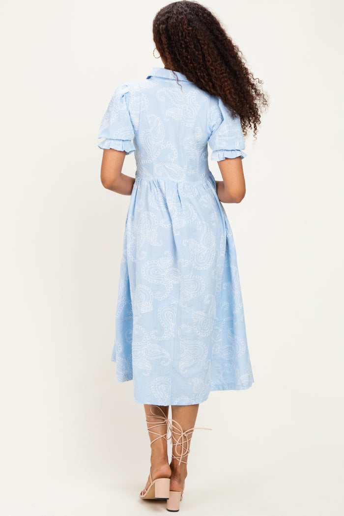 woman wearing a light blue paisley print midi dress with puff sleeves and a belted waist, viewed from the back