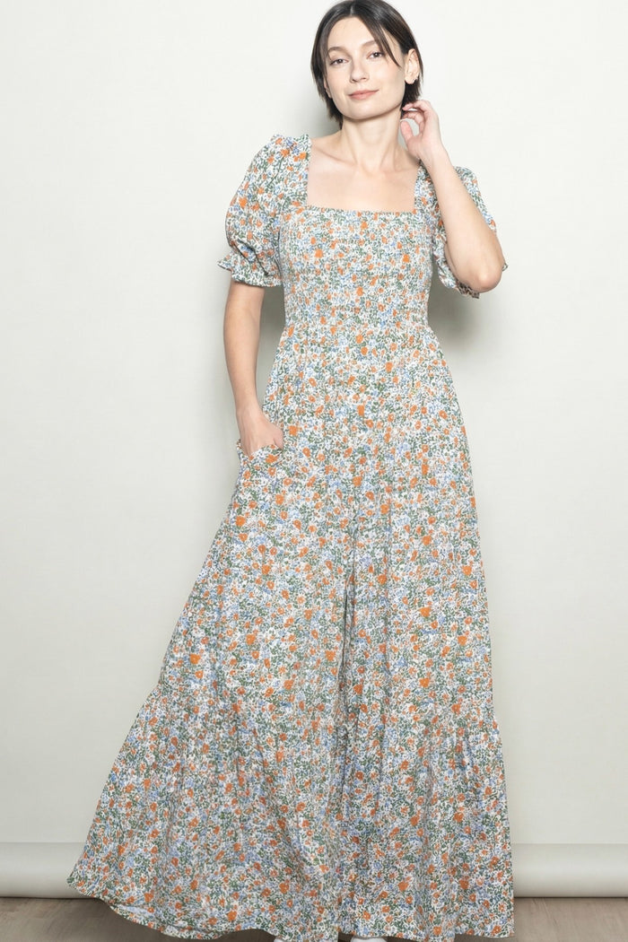 woman wearing a floral maxi dress with puff sleeves and pockets, standing against a light background