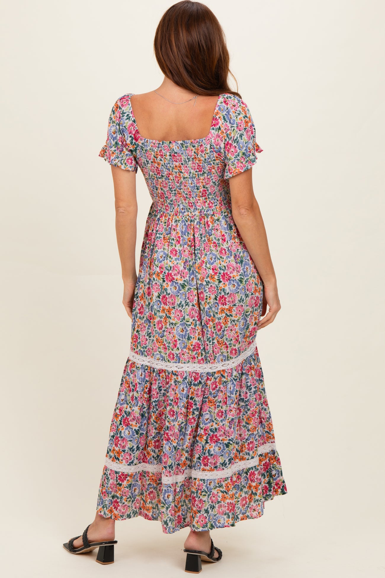 woman wearing a colorful floral maxi dress with short puff sleeves and a tiered skirt, shown from the back