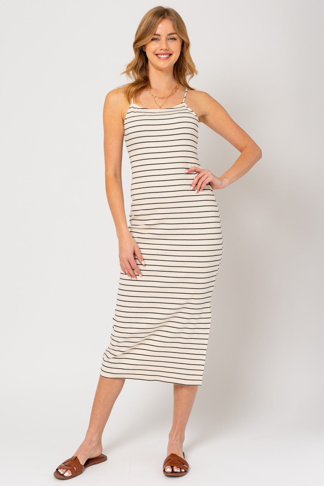 woman wearing a beige and black striped midi dress with spaghetti straps and standing with one hand on her hip
