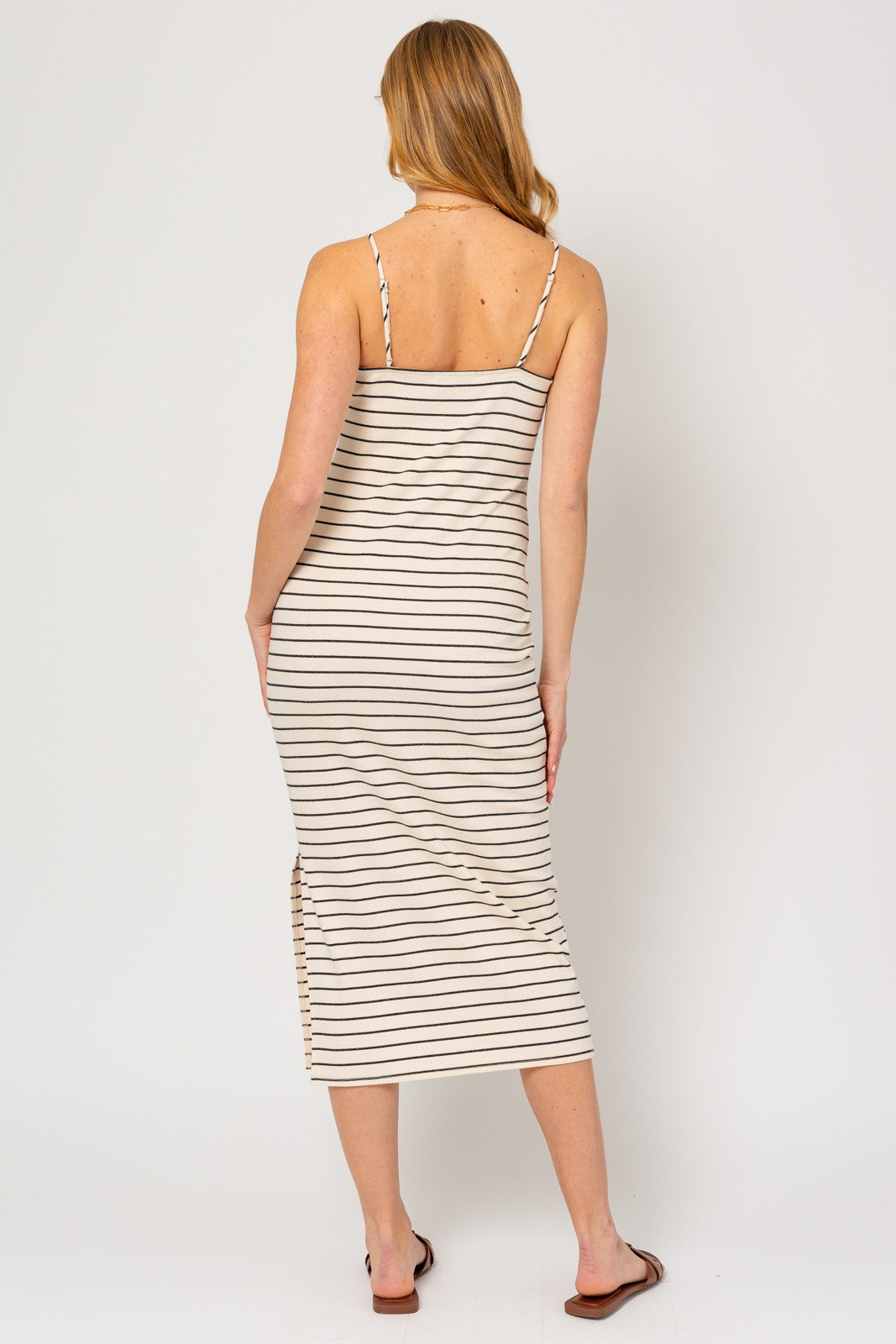 woman wearing a beige and white striped midi dress with spaghetti straps and a side slit, seen from the back