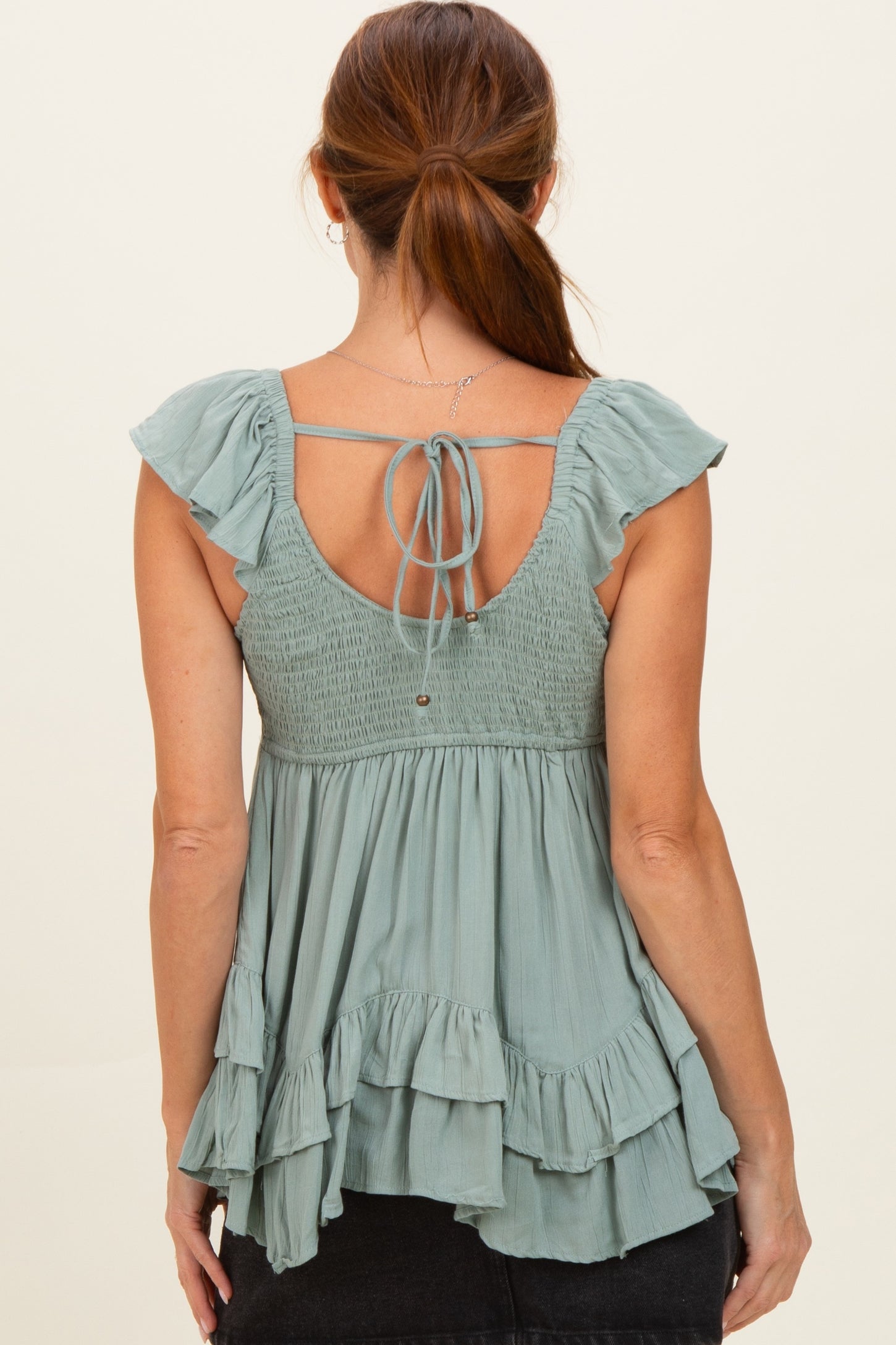 woman wearing a soft green maternity top with ruffled sleeves and a tie-back detail, showcasing a flowy design