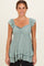 woman wearing a light green maternity top with ruffled sleeves and a tiered hem, posing and smiling at the camera