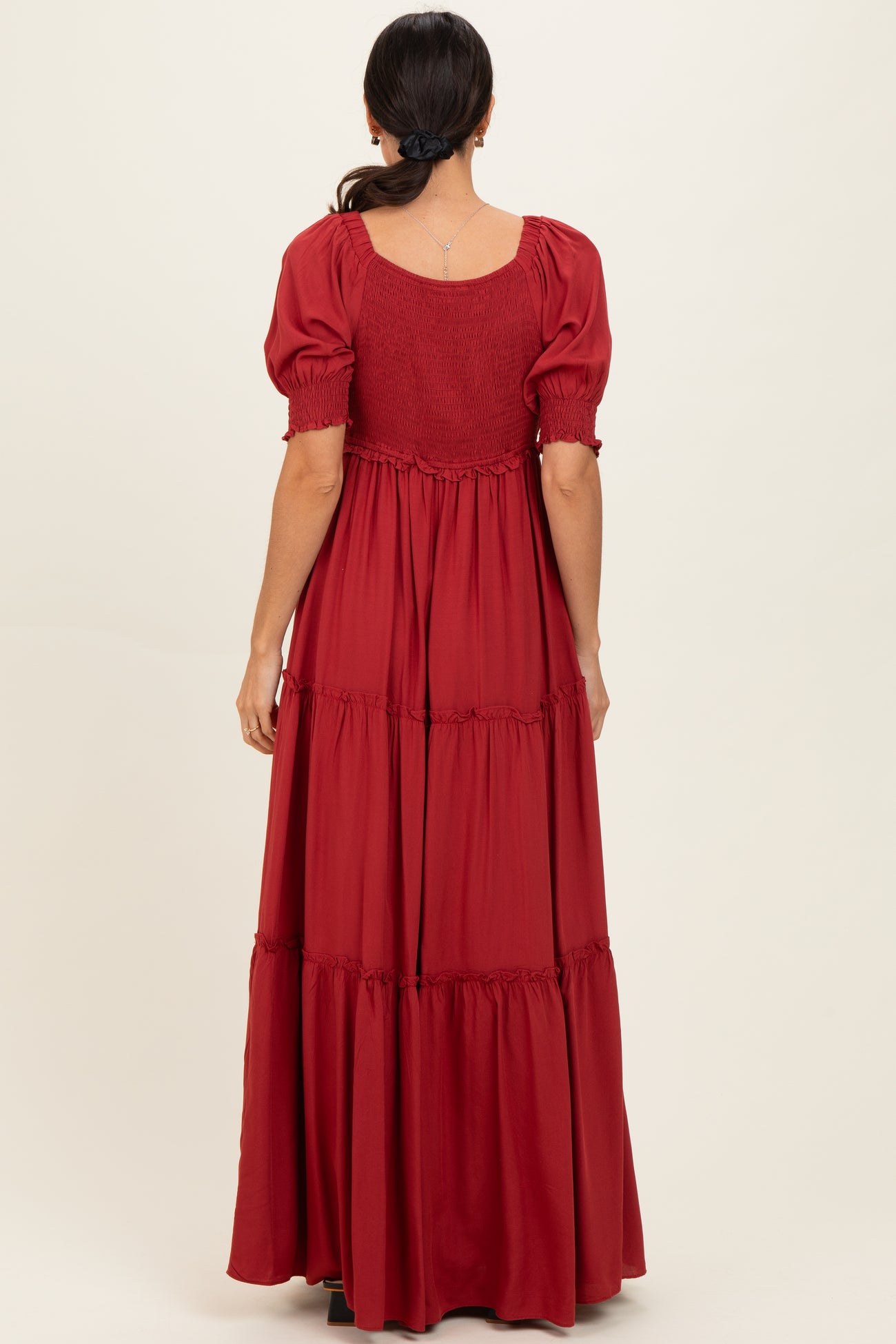 woman wearing a burgundy tiered maxi dress with short puff sleeves and a smocked bodice, shown from the back