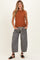 woman wearing an orange sleeveless maternity top and loose black and white striped maternity pants with pockets