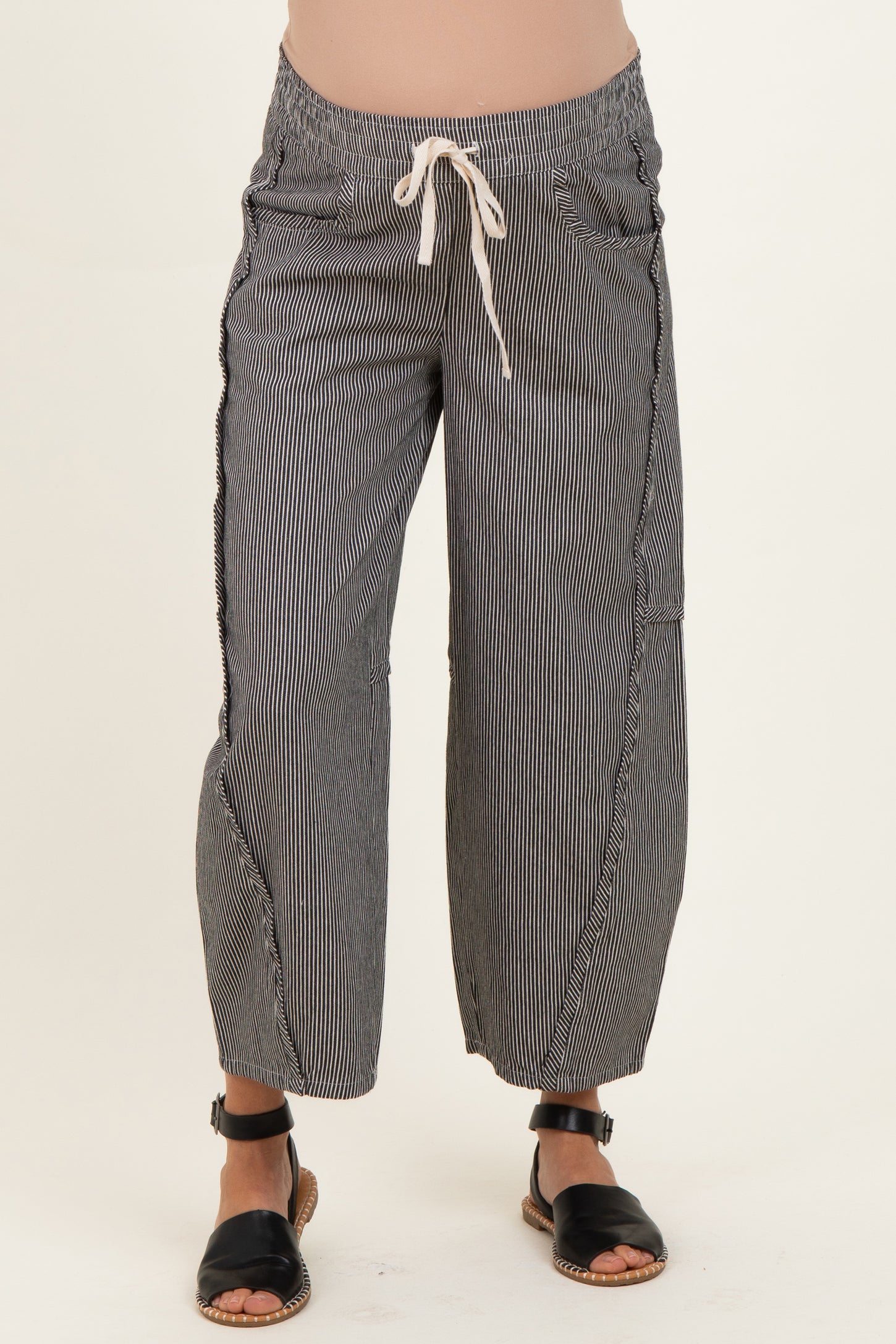 woman wearing black and white striped maternity pants with a drawstring waist and cropped length, showcasing her baby bump