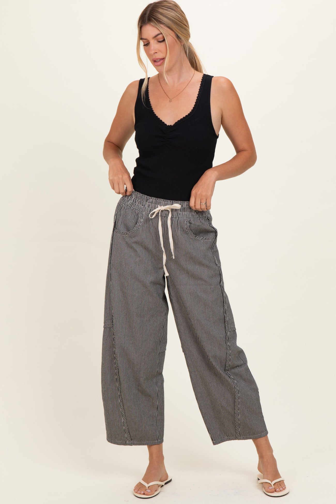 woman wearing a black sleeveless top and black and white striped wide-leg pants with a drawstring waist