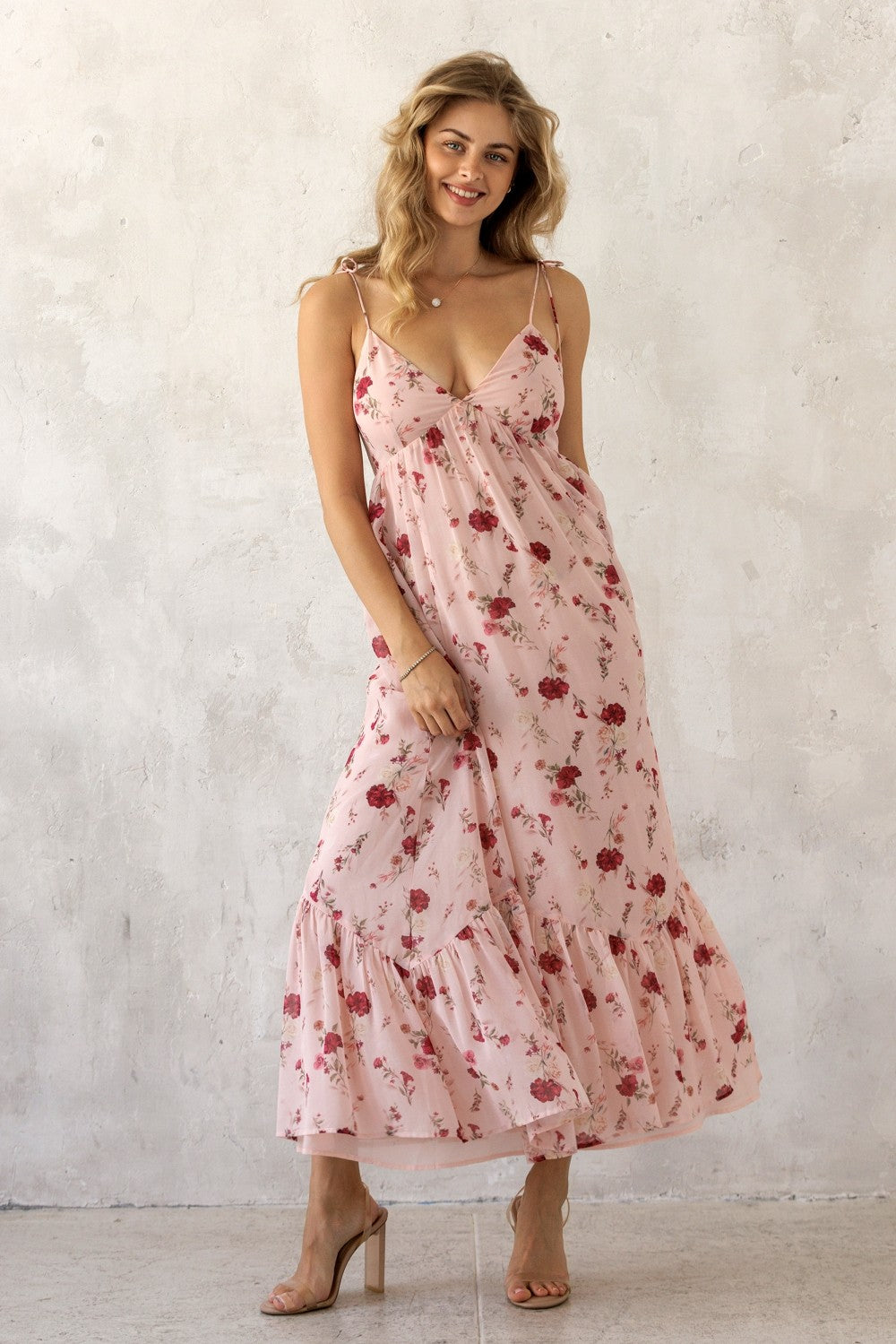 woman wearing a pink floral maxi dress with adjustable straps and a tiered skirt, standing against a neutral background