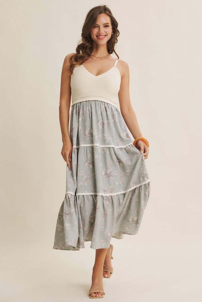 woman wearing a light grey floral maxi dress with a white bodice and tiered skirt, smiling and holding an orange