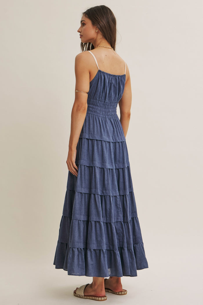 woman wearing a tiered denim maxi dress with a smocked bodice and spaghetti straps, viewed from the back