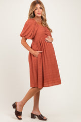 woman wearing a burnt orange maternity dress with short puff sleeves and pockets, showing her baby bump