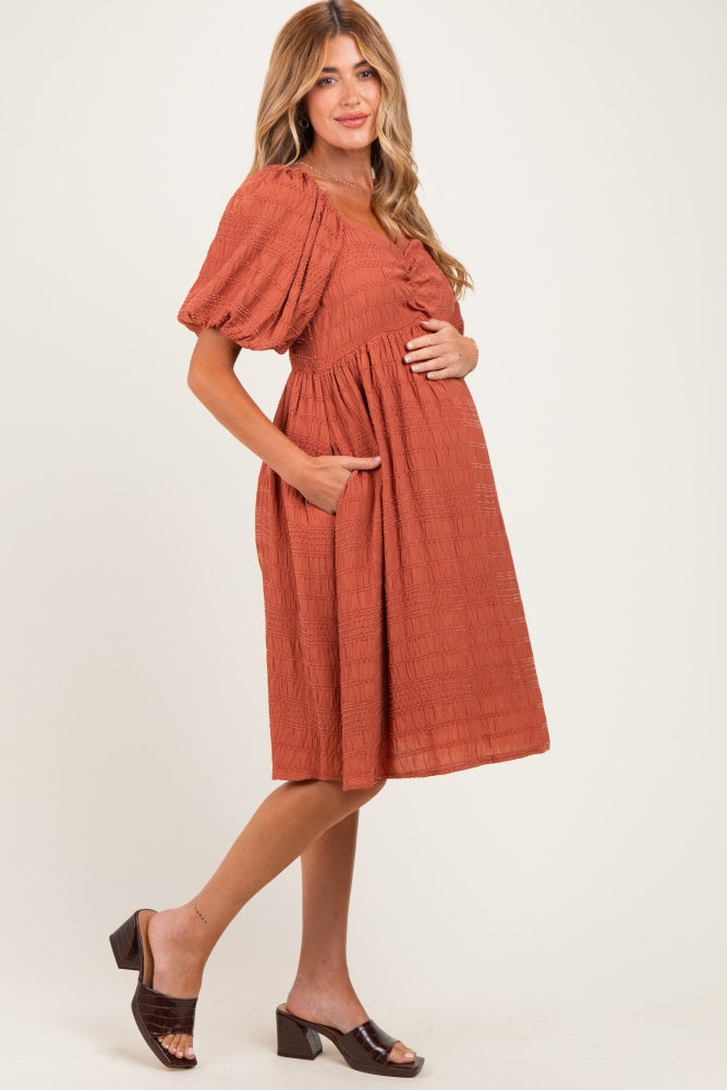 woman wearing a burnt orange maternity dress with short puff sleeves and pockets, showing her baby bump