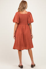 woman wearing a rust-colored maternity dress with puff sleeves and a smocked back, view from the back