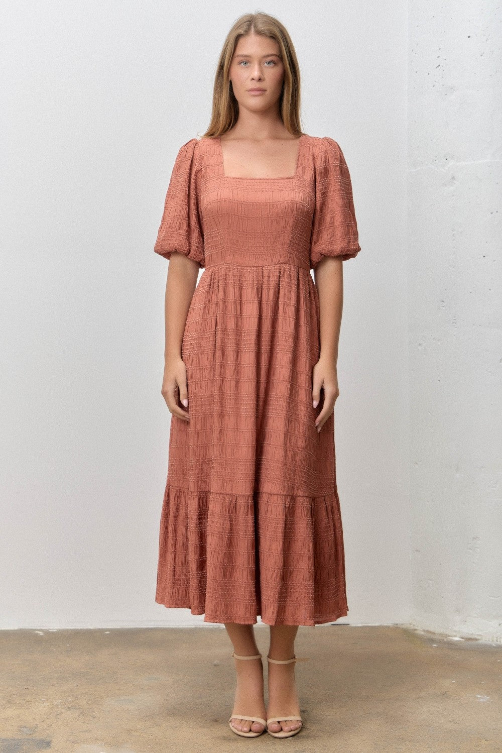 woman wearing a rust-colored midi dress with puff sleeves and a square neckline