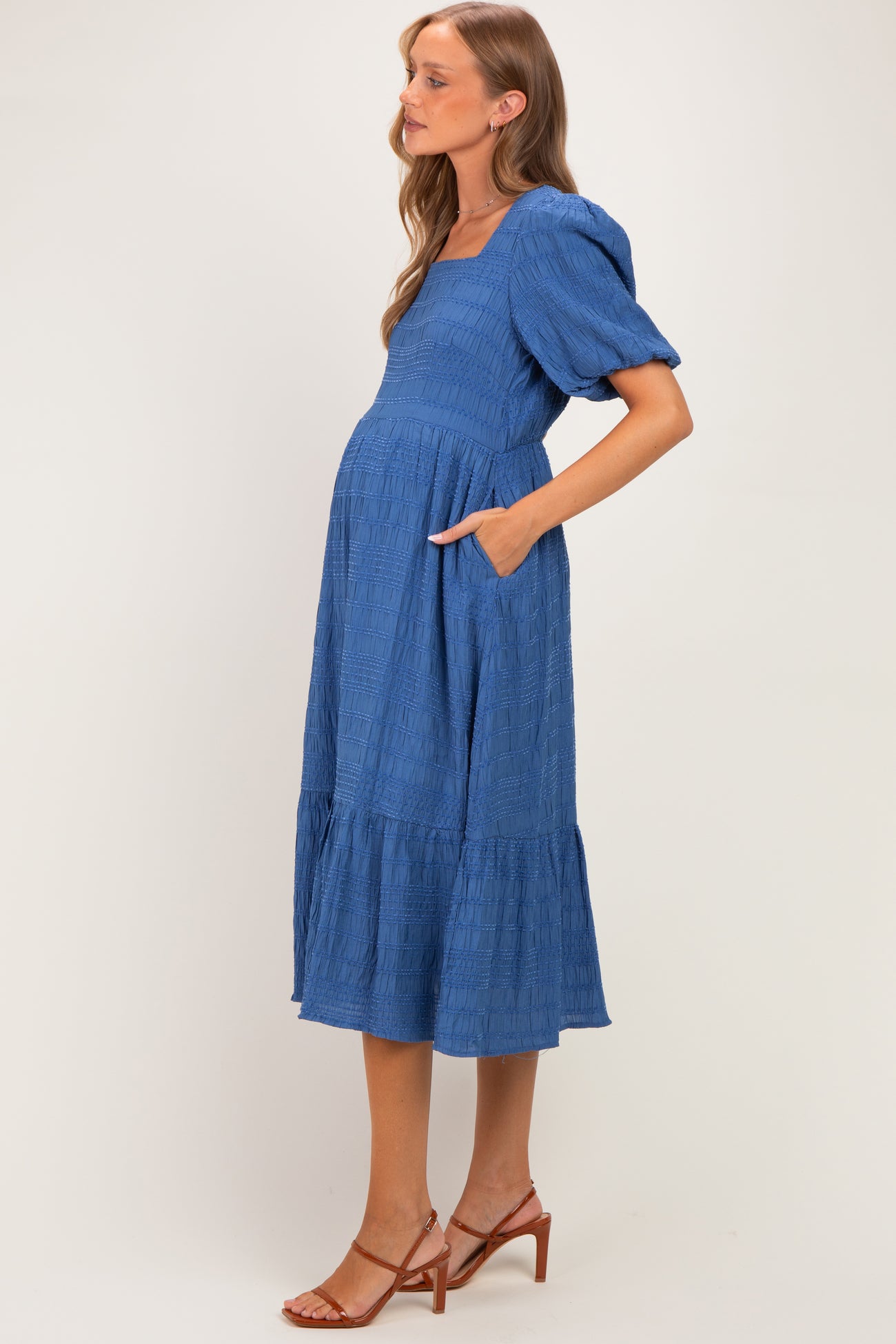 woman wearing a blue midi maternity dress with puff sleeves and pockets, and a visible baby bump