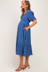 woman wearing a blue midi maternity dress with puff sleeves and pockets, and a visible baby bump