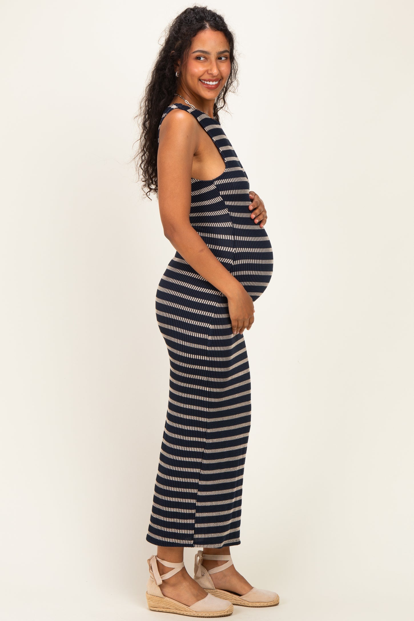 woman wearing a navy and cream striped sleeveless maternity dress, showcasing her baby bump