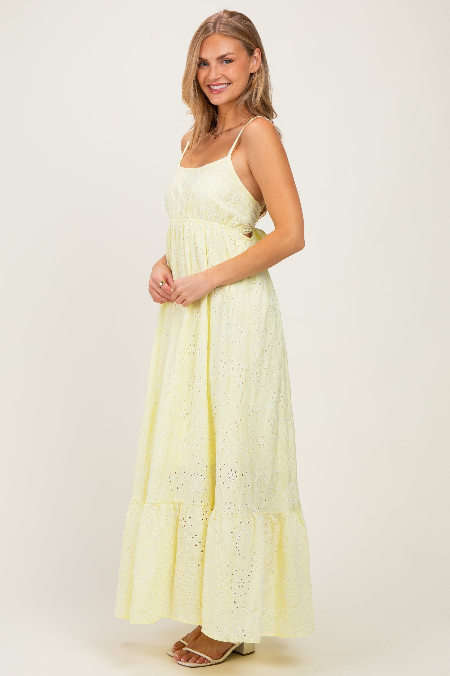 woman wearing a light yellow spaghetti strap maxi dress with eyelet details and a tiered skirt