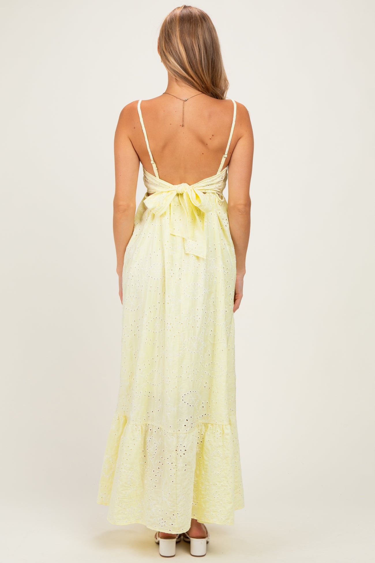 woman wearing a yellow eyelet maxi dress with a back tie detail and ruffled hem
