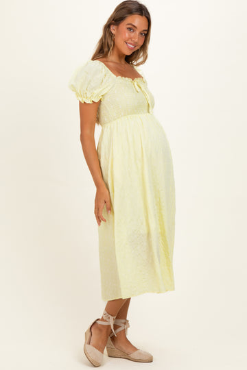 woman wearing a yellow puff sleeve maternity dress with a cinched bodice and a visible baby bump