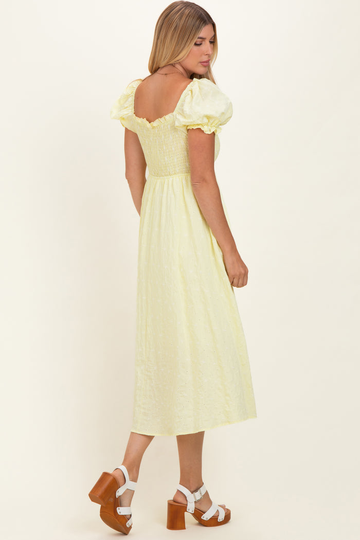 woman wearing a yellow puff sleeve midi dress with a smocked bodice and a flowy skirt, standing against a light background