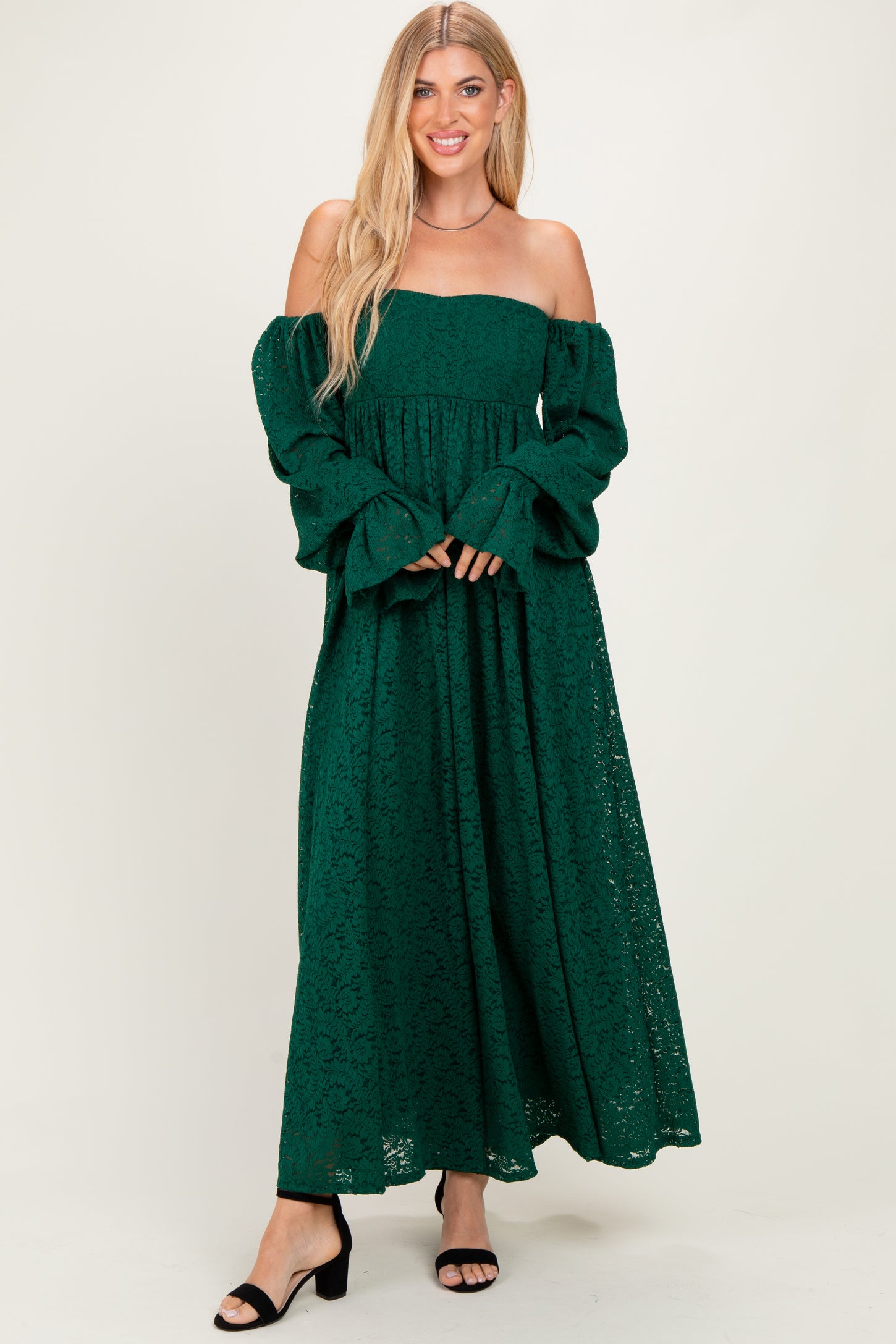 woman wearing a dark green off-the-shoulder lace maxi dress with long bell sleeves and a flowy skirt