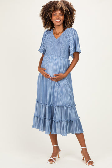 woman wearing a light blue maternity dress with a smocked bodice and ruffled hem, holding her baby bump